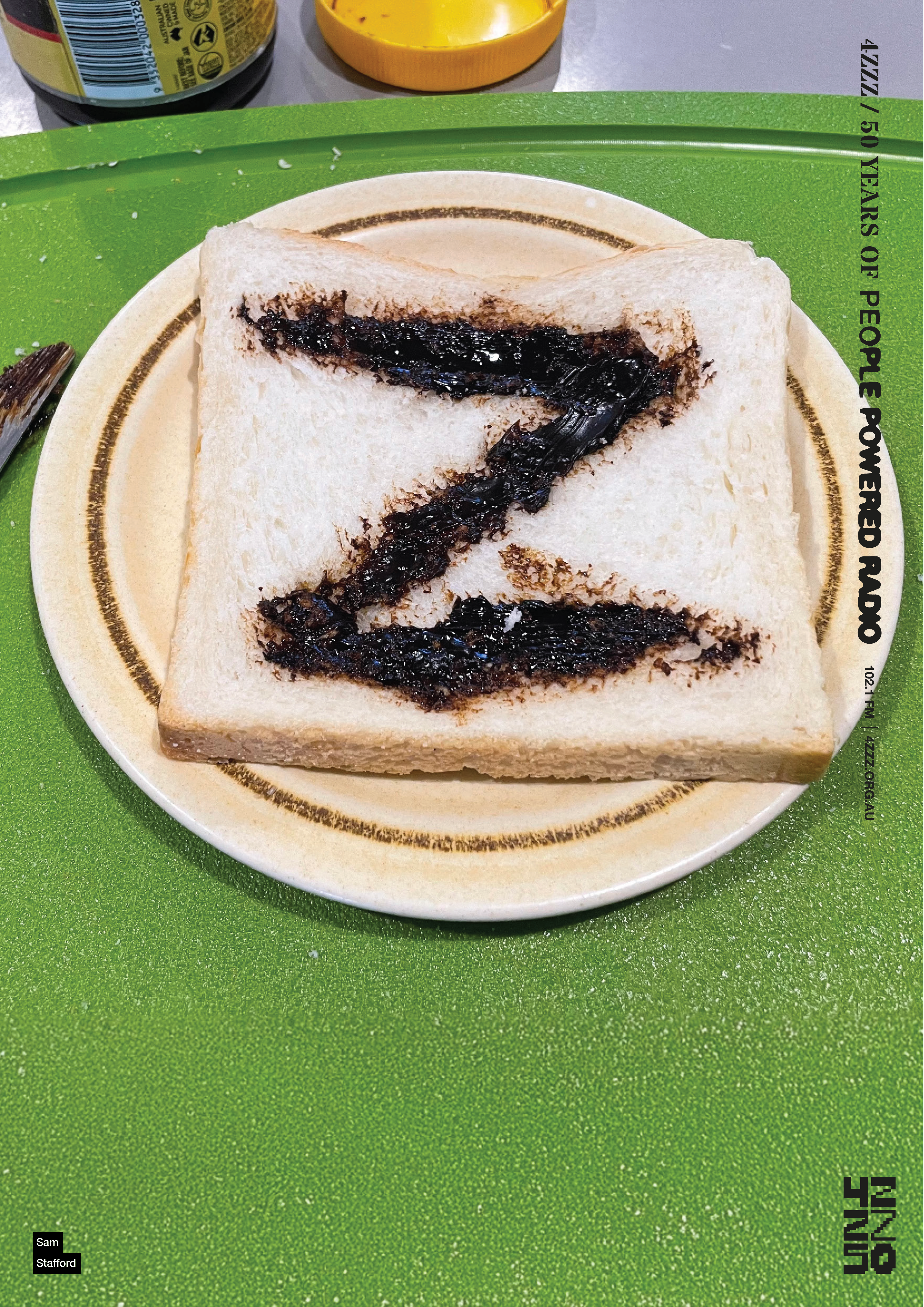 a piece of white bread with a vegemite smear in the shape of a Z. The bread is on a white and brown plate, on a green table.