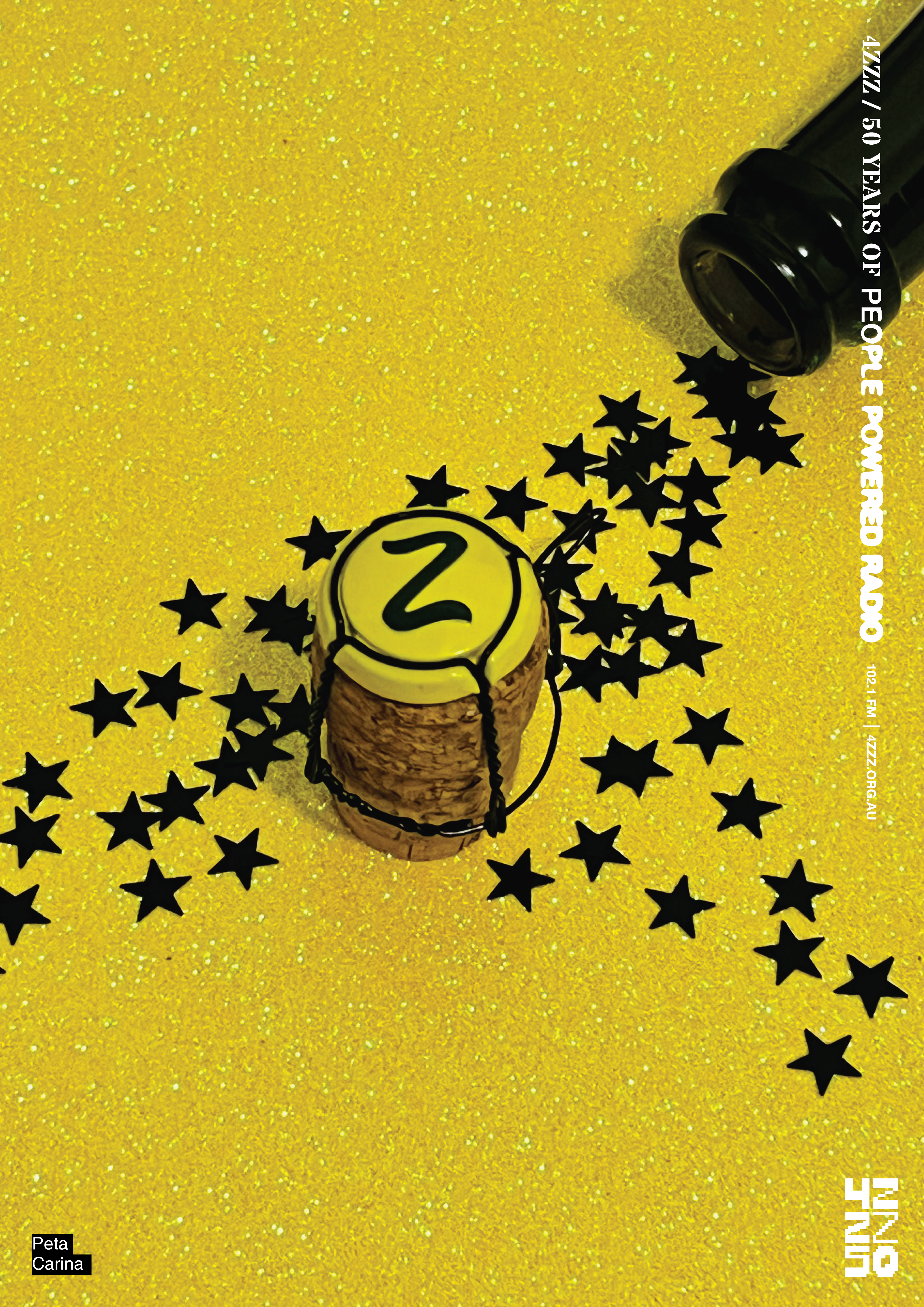 a yellow sheet with a champagne cork and bottle on top. Black star shaped confetti 'pours' out of the bottle, and the cork is topped with a yellow cap emblazoned with a Z.