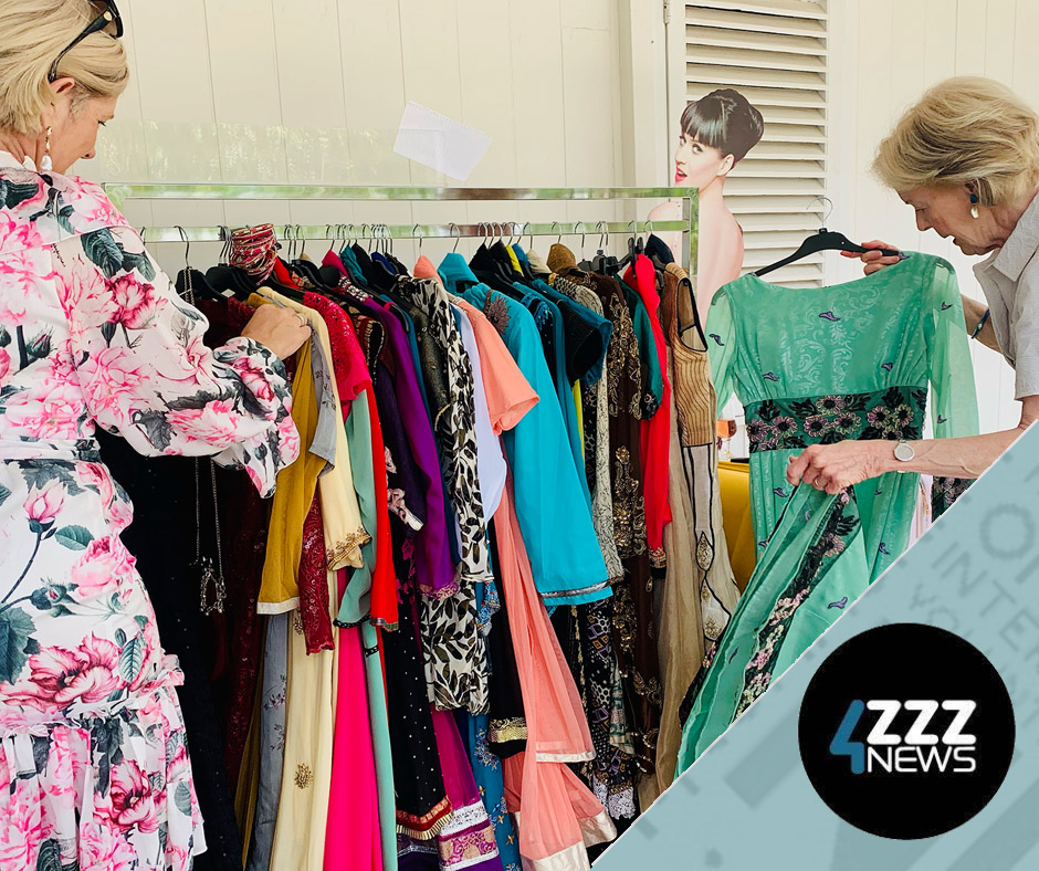 Two women admire a clothing rack of dresses 
