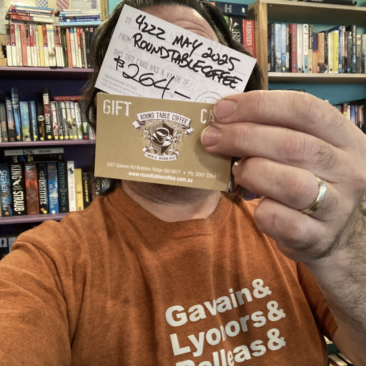 Person in orange t shirt holds up a voucher for Round Table Coffee in front of his face.