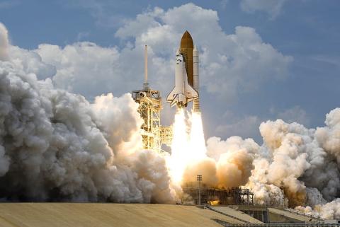 a photo of a rocket ship in the process of launching surrounded by black smoke. 