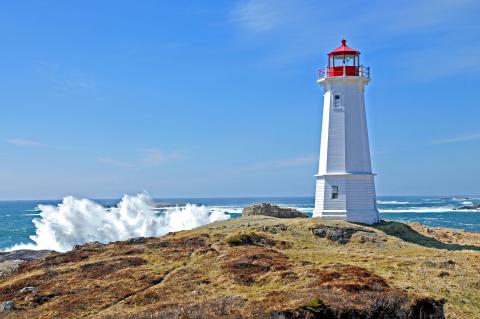 A lighthouse on the island as waves crash along the rocks.