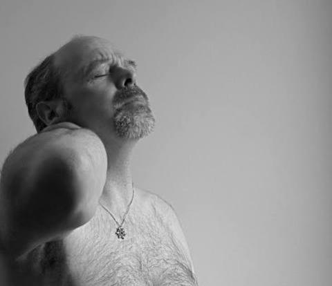 A man with his arm around the back of his neck with a pained expression.