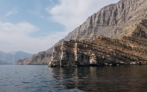 A cliff sitting along the Strait of Hormuz, with a view of a ledge behind it going into the horizon.
