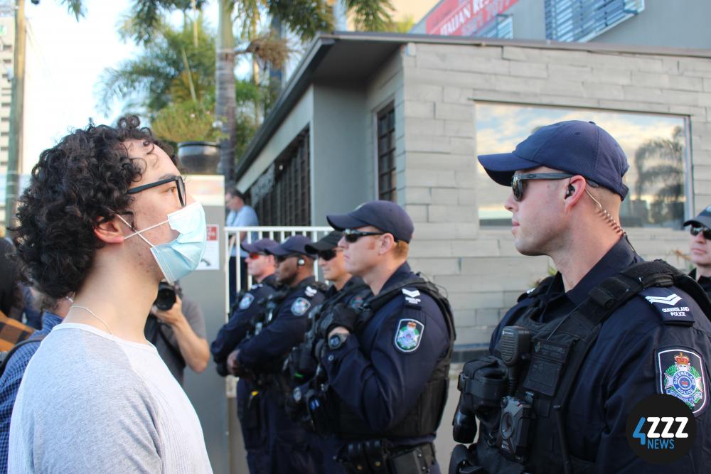 A protester stands silently in front of police, as they block off access to the hotel entrance. [4ZZZ/Lillian Rangiah]