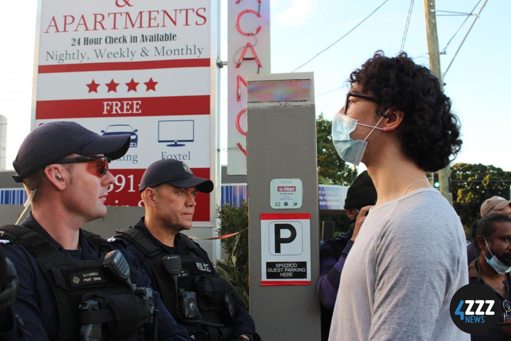 As Media take photos, the original officer swaps places with another officer. [4ZZZ/Lillian Rangiah]