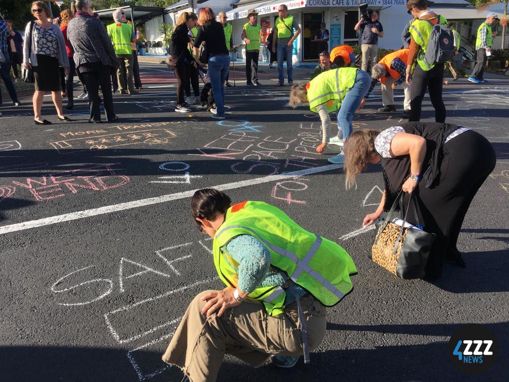 A group of people write messages about road safety with chalk on Montague Road in West End