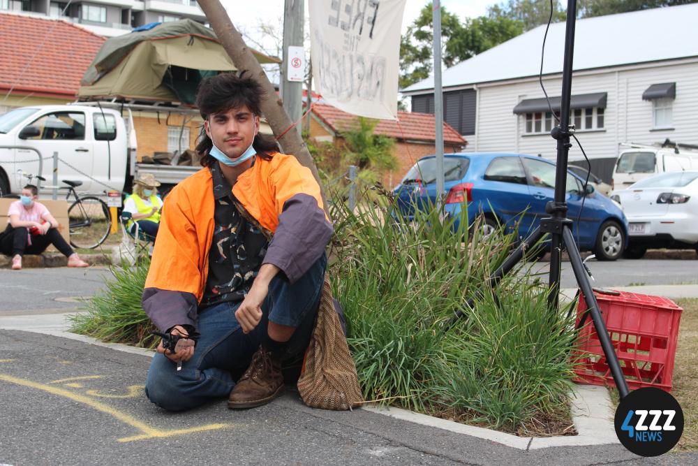 A protest marshal keeps an eye on the footpath, more blockaders have set up for overnight camping behind him. [4ZZZ/Lillian Rangiah]