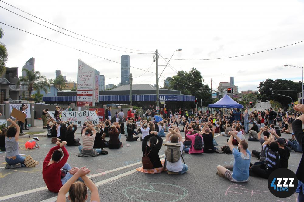 Protesters on Main St. cross their arms above their head in a show of solidarity with detainees. [4ZZZ/Lillian Rangiah]