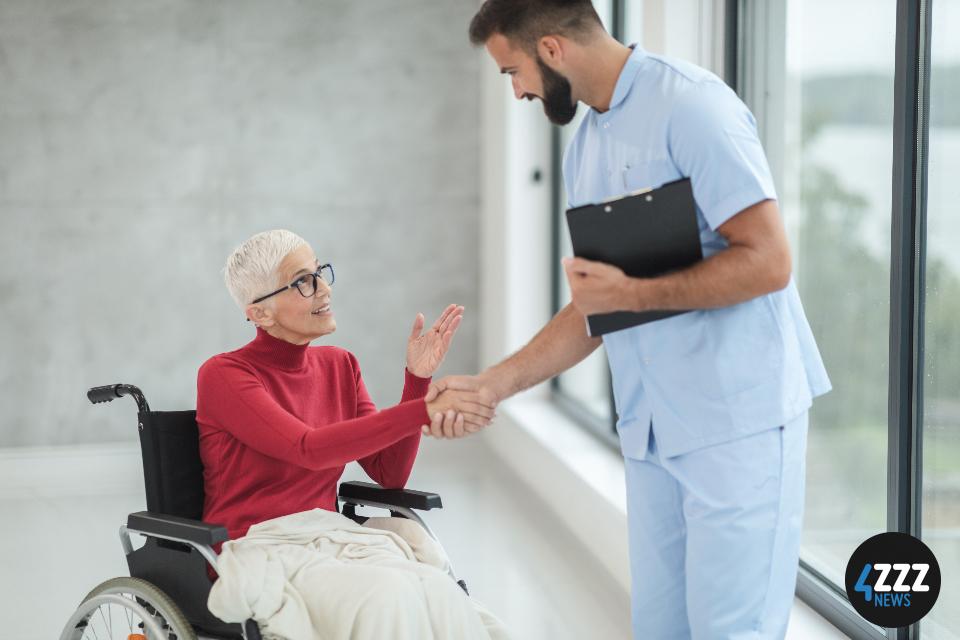 Nurse shaking the hand of a patient sitting in a wheelchair.