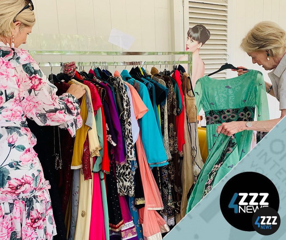 Two women admire a clothing rack of dresses 